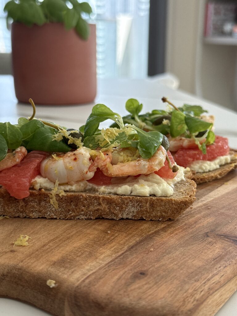 With marinated shrimp, grapefruit, mâche salad, capers, and creamy goat cheese
Let’s take a simple toast and turn it into a light yet luxurious starter. Juicy shrimp, zesty citrus, creamy melted goat cheese, peppery greens, and a little crunch from capers — all packed into one perfect bite.

