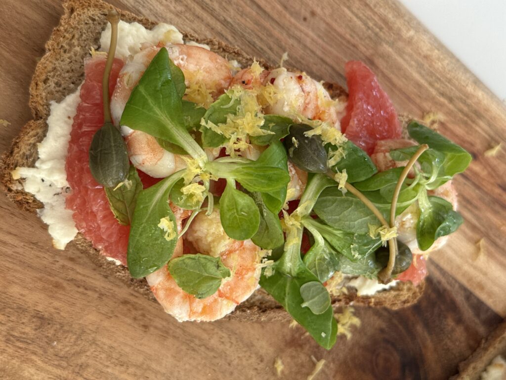 With marinated shrimp, grapefruit, mâche salad, capers, and creamy goat cheese Let’s take a simple toast and turn it into a light yet luxurious starter. Juicy shrimp, zesty citrus, creamy melted goat cheese, peppery greens, and a little crunch from capers — all packed into one perfect bite.
